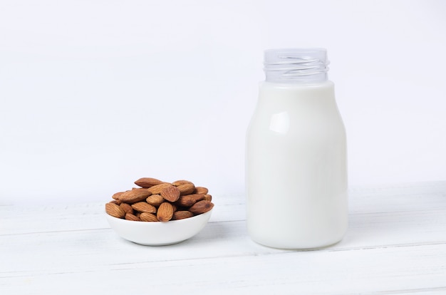 Almond milk in bottle with nuts on white surface