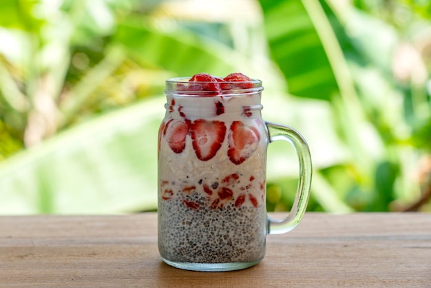 Almond milk chia pudding with fresh red strawberries goji berries and oat flakes in a glass jar mug Vegan raw breakfast Chia seeds and fresh cut fruits and berries dessert