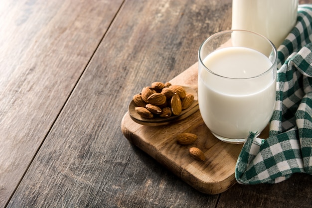 Almond milk in glass and bottle on wooden table. Copy space