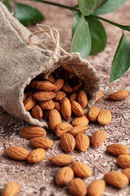 Almonds are scattered on the table In the background is a bag of almonds and green leaves Brown background Closeup