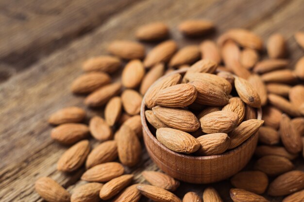 Almonds in brown bowl on wooden background