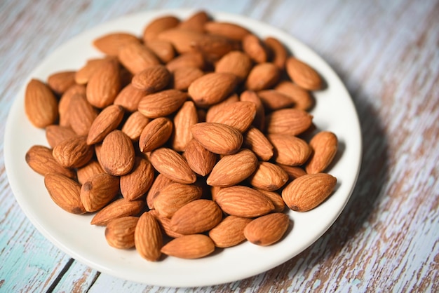 Almonds nuts on white palte Delicious sweet almonds on the wooden table background roasted almond nut for healthy food and snack