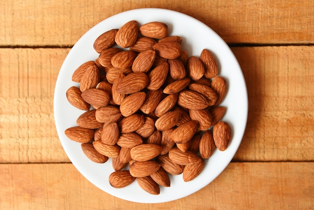 Almonds nuts on white plate on wooden background. Roasted almond for snack