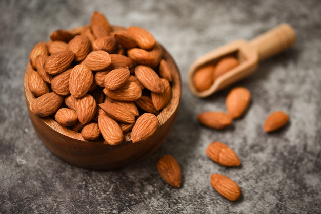 Photo almonds nuts on wooden bowl on dark wall , top view - roasted almond for snack