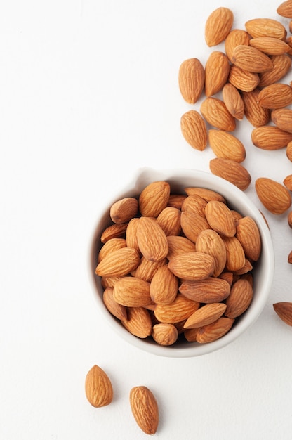 Almonds in a white cup. Nearby is a group of almonds. White background. View from above. Place for your text.