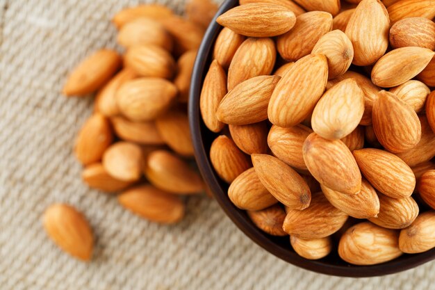 Almonds in a wooden cup on a burlap cloth background