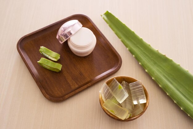 Aloe vera cosmetic cream on wooden tray with aloe leave and bowl on light background