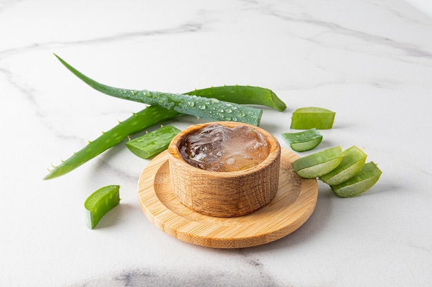 Aloe vera gel in a wooden bowl on a marble background with leaves and slices of fresh aloe the concept of skin care of the face body hair