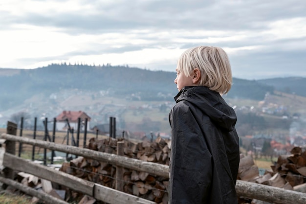 Alone blond teenage boy outside on the village in the mountains background Travel Lifestyle Schoolboy walks outside