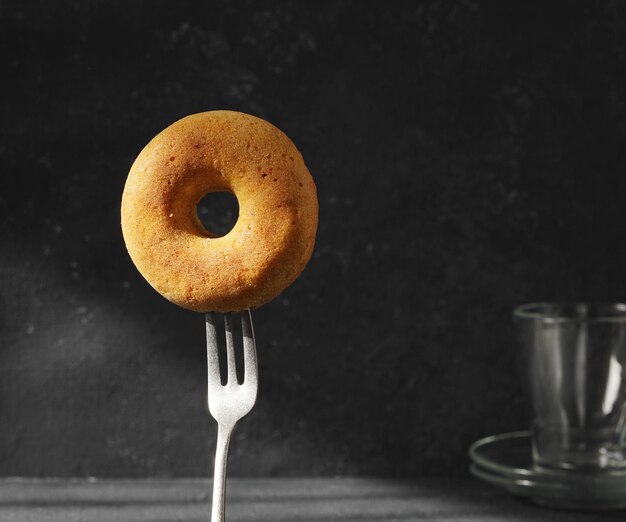 Alone Donut on the fork in the sun rays on the dark background copy space