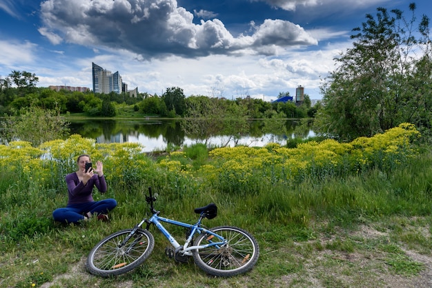 Alone girl talks online over a video link near her bicycle in a city park. Keeping distance during the coronavirus pandemic.