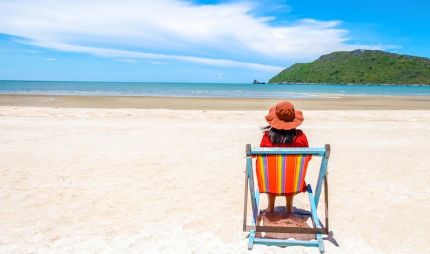 Alone woman relaxing on a wooden chair at a tropical beach enjoying the sea and sky