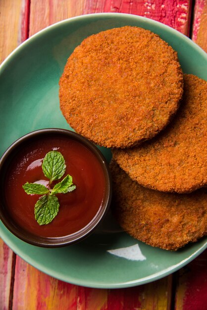 Aloo Tikki or Patties or Cutlet is a popular snack or snack from India, Served with Tomato Ketchup or Imli chutney over moody background. Selective focus