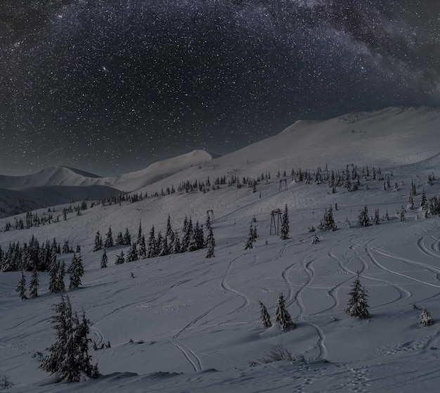 Alpine resort ski lift with seats going over night mountain skiing freeride slopes and fir tree groves Milky Way Galaxy stars above Svydovets ridge view from Dragobrat ski resort