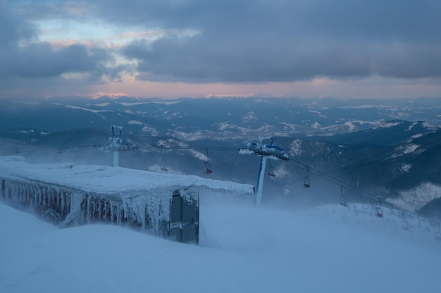 Alpine resortr ski lift with seats going over the sunset mountain skiing slopes in extremally windy weather