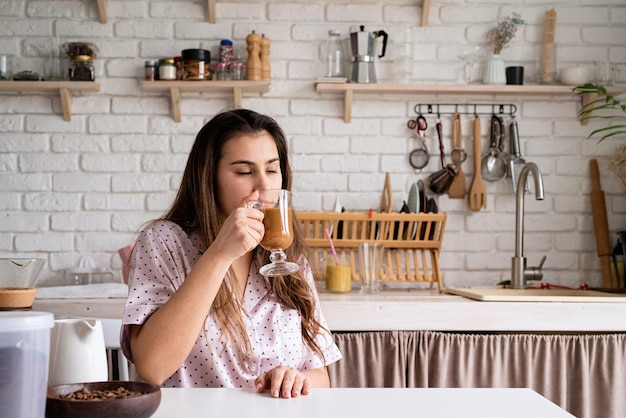 Alternative coffee brewing young woman in lovely pajamas drinking coffee with milk at home kitchen