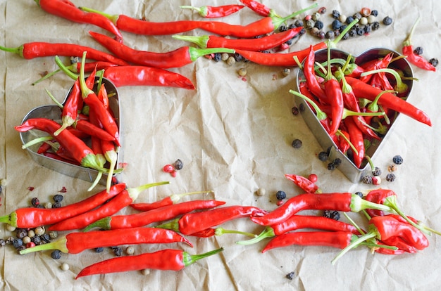 Aluminum heart shapes filled with little chili peppers on vintage paper background