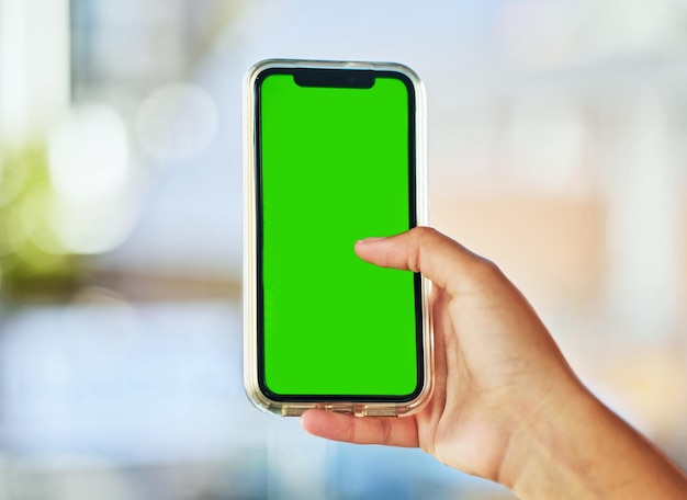 Always connected A young woman holding up a smartphone with a green screen against a defocused background