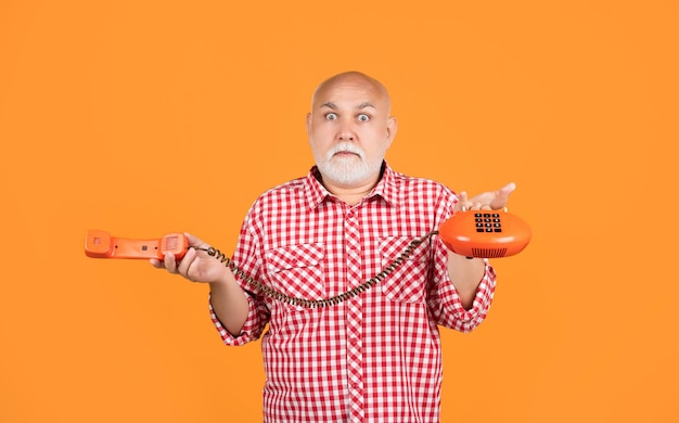 Amazed aged man with retro telephone on yellow background