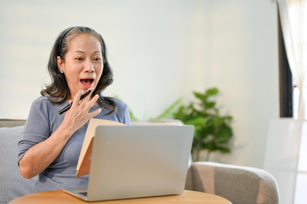 Amazed Asianaged retired woman covering her mouth looking at her laptop screen