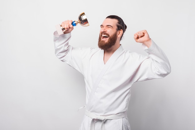 Amazed bearded fighter taekwondo man holding gold cup and celebrating