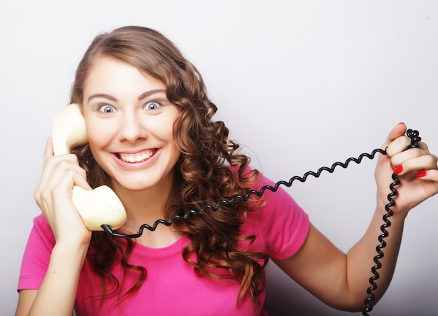 Amazed beautiful curly woman talking on white vintage telephone isolated over white background