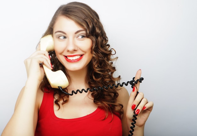 Amazed beautiful curly woman talking on white vintage telephone isolated over white background