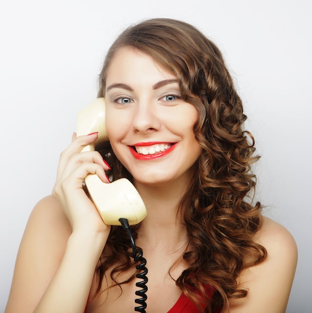 Amazed beautiful curly woman talking on white vintage telephone isolated over white background