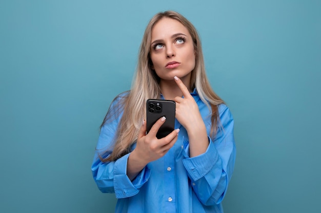 Amazed carefree enchanted blonde woman with a smartphone in her hands on a blue bright background