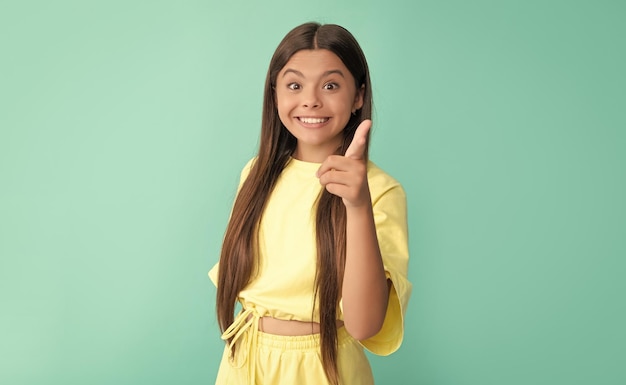 Amazed child with long hair pointing finger on blue background advertising