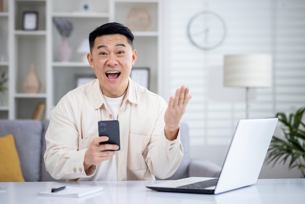 Amazed eastern man using cellular phone while sitting in remote workspace with personal computer and