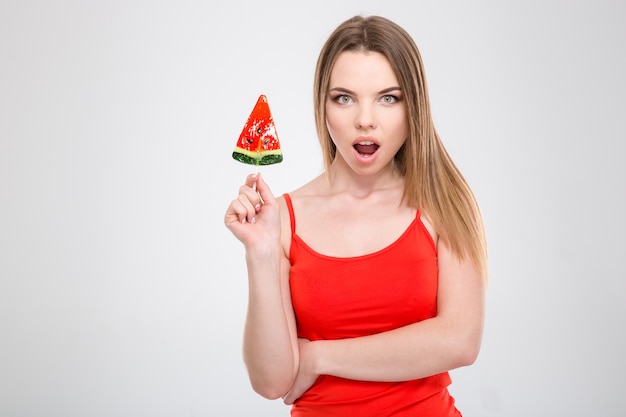 Amazed excited wondered young female holding red sweet tasty watermelon shaped lollypop