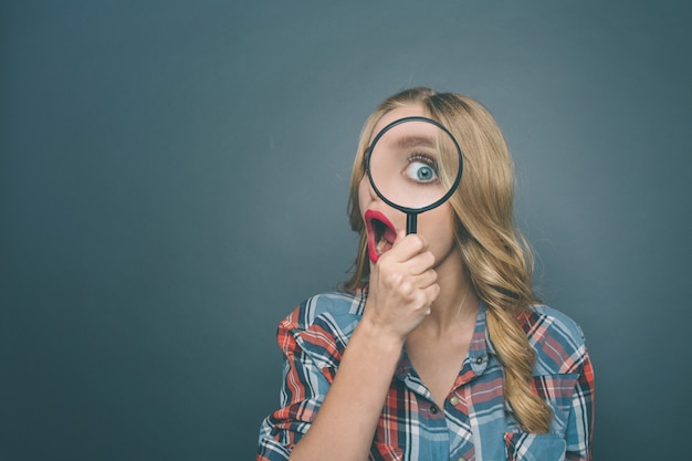 Amazed girl is looking through magnifying glass and wondering