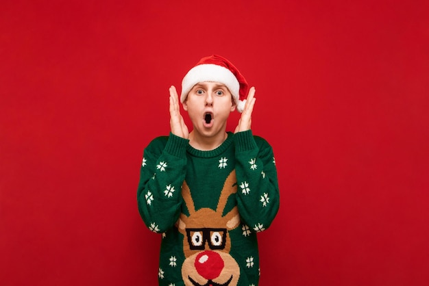 Amazed guy in santa hat isolated on red background