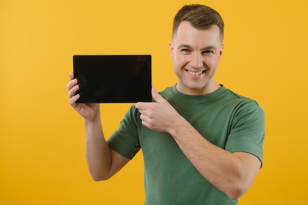 Amazed happy man using digital tablet looking shocked about social media news astonished man shopper consumer surprised excited by online win isolated over yellow background