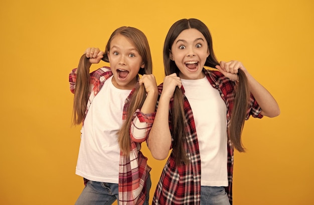 Amazed kids in casual checkered shirt hold long straight hair on yellow background hairstyle