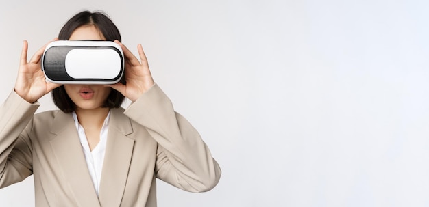 Amazed office woman asian business person in suit wearing vr headset looking at smth in virtual reality glasses with impressed wow face white background