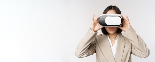 Amazed office woman asian business person in suit wearing vr headset looking at smth in virtual reality glasses with impressed wow face white background