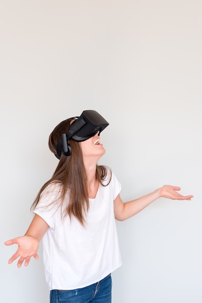 Photo amazed positive woman wearing virtual reality goggles headset, vr box. connection, technology, new generation, progress concept. girl surprised by something in virtual reality. studio shot on gray