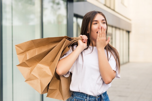 Amazed shopper opening mouth holding shopping bags watching special offers in stores and pointing in the street