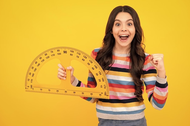 Amazed teenager School girl holding measure for geometry lesson isolated on yellow background