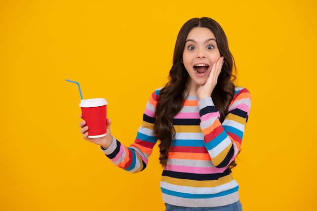 Amazed teenager Teenager girl holding a hot cup of coffee or tea Child with takeaway cup on yellow background morning energy drink beverage Excited teen girl