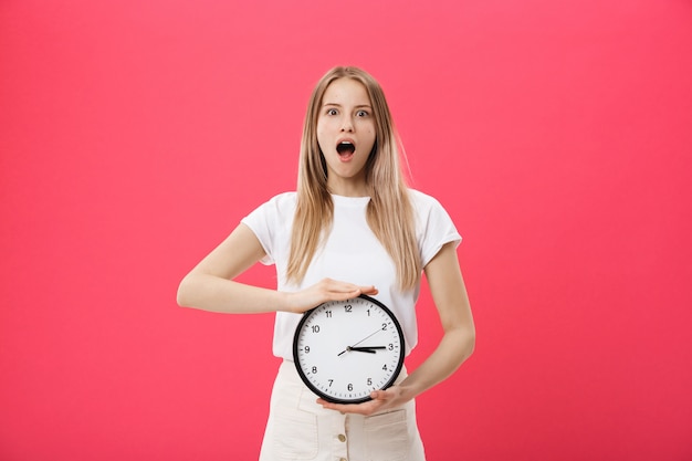 Amazed woman holding clock. Surprised woman in white t-shirt holds black clock