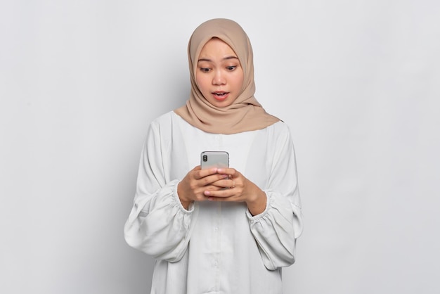 Amazed young Asian Muslim woman using a mobile phone received good news isolated over white background