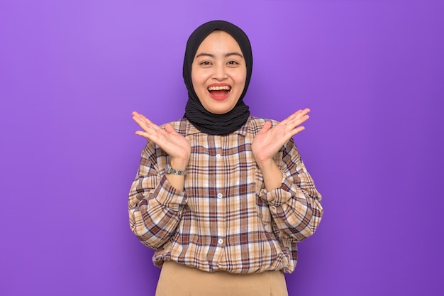 Amazed young Asian woman in plaid shirt looking at camera with wow face expression isolated on purple background