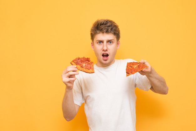 Amazed young man on a yellow background,holding two pieces of pizza in his hands