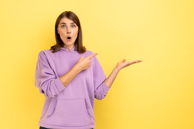 Amazed young woman pointing at copy space on her palm empty place for idea presentation