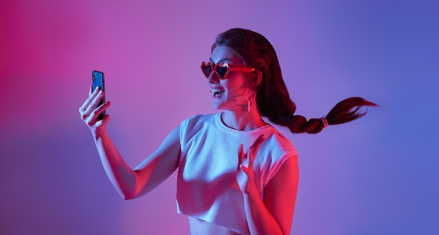 Amazed young woman using mobile phone on neon background digital media technology 5g concept