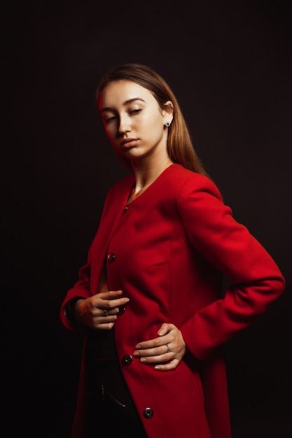 Amazing brunette woman with natural makeup and shiny hair posing in trendy red coat at studio