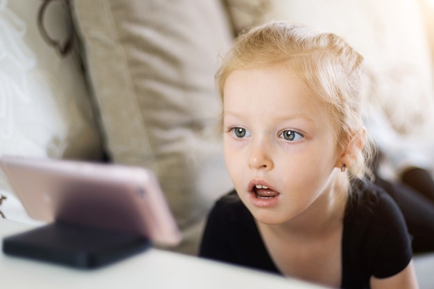 Amazing little girl look at phone. Child watching online cartoons, kids computer addiction, parental control concept.